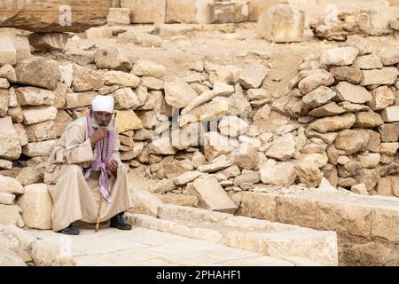 Un vecchio uomo locale seduto su una roccia presso il complesso delle Piramidi di Giza in Egitto Foto Stock