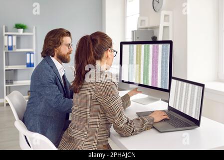 I colleghi d'affari stanno lavorando insieme in ufficio con fogli di calcolo sugli schermi dei computer. Foto Stock