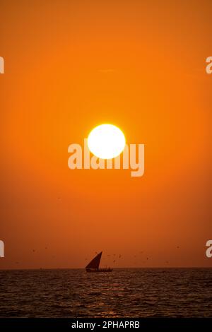 Una piccola barca a vela che si affaccia su un tramonto mozzafiato sul mare aperto Foto Stock
