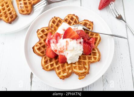 Waffle con panna montata e guarnizione di fragola su un piatto dall'alto Foto Stock