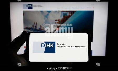 Persona che tiene in mano uno smartphone con il logo di Deutsche Industrie- und Handelskammer (DIHK) sullo schermo davanti al sito Web. Messa a fuoco sul display del telefono. Foto Stock