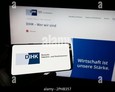 Persona che tiene un telefono cellulare con il logo di Deutsche Industrie- und Handelskammer (DIHK) sullo schermo davanti alla pagina web. Messa a fuoco sul display del telefono. Foto Stock