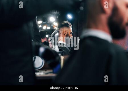 Giovane uomo barbuto seduto e di ottenere taglio di capelli in barbiere Foto Stock