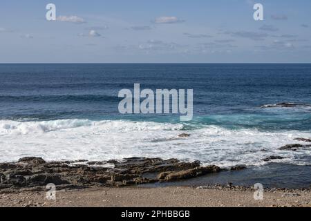 Spiaggia dell'oceano Atlantico con una costa rocciosa. Acqua calma in inverno. Cielo blu con nuvole di luce. Aquas Verdes, Playa del Valle, Fuerteventura, CA Foto Stock