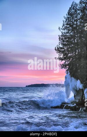 Il surf frigido si aggira sulla costa ghiacciata del Lago superiore sotto un cielo al tramonto dipinto in vivaci tonalità rosa e magenta Foto Stock