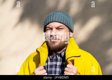 Ritratto dell'uomo bearded che indossa giacca gialla d'inverno e cappello godendo di calde luci del sole di primavera. Foto Stock