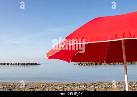 Ombrello sfondo spiaggia. Ombrello Red Beach sullo sfondo dell'Oceano Blu. Paesaggio della spiaggia. Sfondo marino. Colorato design estivo. Preparazione Foto Stock