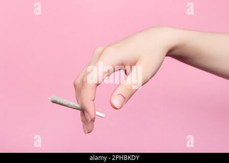 La mano di una donna tiene un'articolazione con la marijuana medica con le dita. Su sfondo rosa Foto Stock