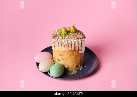 Vita morta con panettone italiano con colorate uova di Pasqua su un piatto di ceramica blu, isolato su sfondo rosa Foto Stock