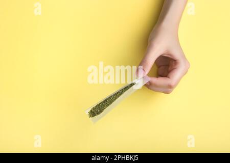 Nelle mani femminili, carta per un'articolazione, un filtro e marijuana medica schiacciata. Su uno sfondo giallo banana brillante Foto Stock
