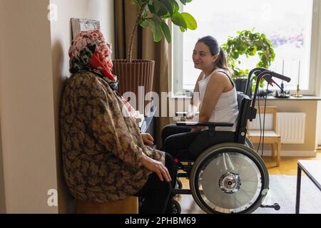 Vista laterale di una donna con paraplegia che parla con la madre a casa Foto Stock