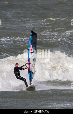 Windsurf ricreativo in muta nera praticando il windsurf classico lungo la costa del Mare del Nord in condizioni di vento durante la tempesta invernale Foto Stock