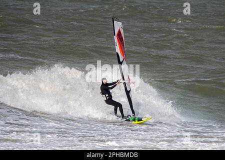 Windsurf ricreativo in muta nera praticando il windsurf classico lungo la costa del Mare del Nord in condizioni di vento durante la tempesta invernale Foto Stock