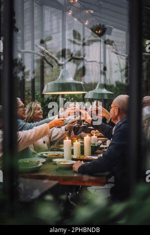 Amici di sesso maschile e femminile che tostano bevande durante la cena in festa cortile Foto Stock
