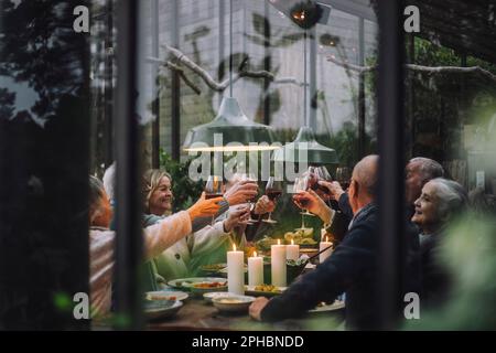 Felice anziano amici maschi e femmine brinda vino durante la festa a cena nel cortile Foto Stock