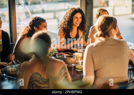Giovane donna che ride con le amiche durante la colazione al centro di ritiro Foto Stock