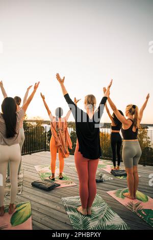 Donne con le braccia alzate praticare yoga sul patio al tramonto Foto Stock