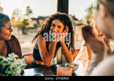 Donna felice che si appoggia sui gomiti mentre parla con le amiche al centro di ritiro Foto Stock