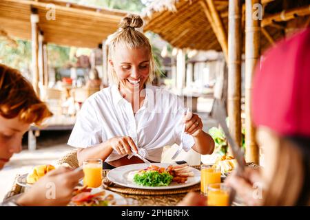 Donna sorridente che fa colazione con figlio a tavola in località turistica durante le vacanze Foto Stock