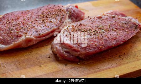 Pezzi di carne cruda cosparsi di sale e spezie su un tagliere. Cottura di costolette di maiale. Foto Stock