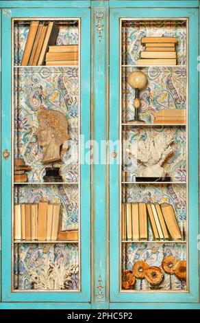Facciata di una libreria d'epoca con una superficie verde scabra, porte in vetro trasparente e libri antichi sugli scaffali. Foto Stock