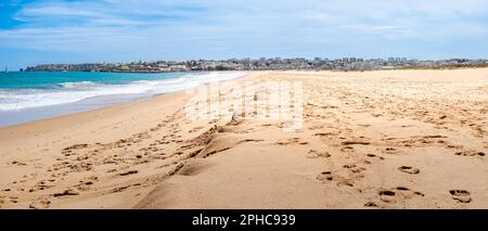 Serena vista panoramica sulla spiaggia di Meia Praia durante la bassa marea, con le splendide scogliere dell'Algarve sullo sfondo e l'affascinante città di Lagos visibile. Foto Stock