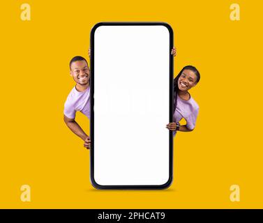 Mockup mobile. Happy Black Couple che guarda fuori dietro lo smartphone Big Blank Foto Stock