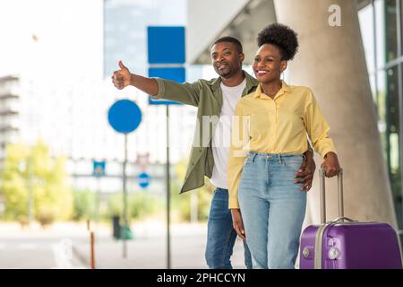 Coniugi neri Taxi Hailing in piedi con Suitcase di viaggio all'aperto Foto Stock