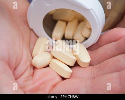 Una donna che versa le compresse di taurato di magnesio da una bottiglia nel palmo della mano. Primo piano. Foto Stock