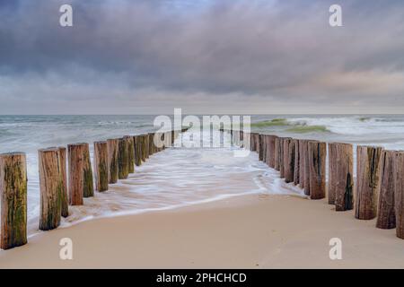 Onde breakers sulla spiaggia di Domburg nei Paesi Bassi. Foto a lunga esposizione con onde dinamiche che si rompono a riva su pali di legno Foto Stock