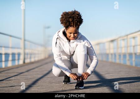 Donna nera sportiva preparandosi per fare jogging all'aperto, Tying Her Shoe Laces Foto Stock