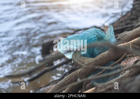 Sacchetto di plastica bloccato sul bordo di un fiume, concetto di inquinamento della natura, immondizia nella natura, copia spazio a sinistra. Foto Stock