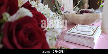 Questa immagine presenta una disposizione floreale bianca e rossa su un tavolo di legno, con pezzi di gioielli assortiti posti sulla superficie del tavolo Foto Stock