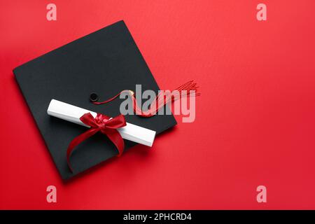 Diploma con nastro e cappello di laurea su sfondo rosso Foto Stock