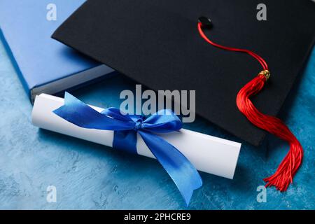 Diploma con nastro, cappello di laurea e libro su tavolo blu Foto Stock
