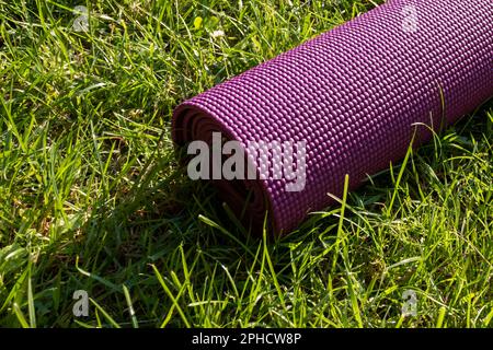 Tappetino da yoga viola su erba verde fresca - concetto di fitness all'aperto Foto Stock