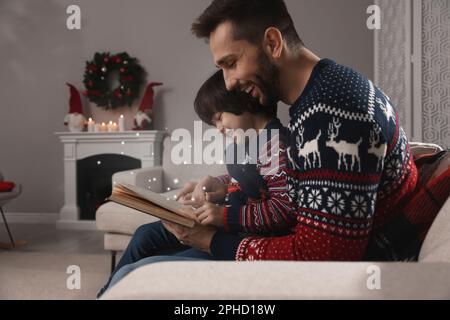 Padre con il suo figlio carino leggere libro in camera decorata per Natale Foto Stock