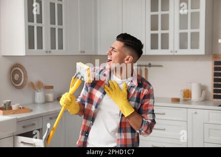 Uomo con il mop che canta mentre pulisce a casa Foto Stock