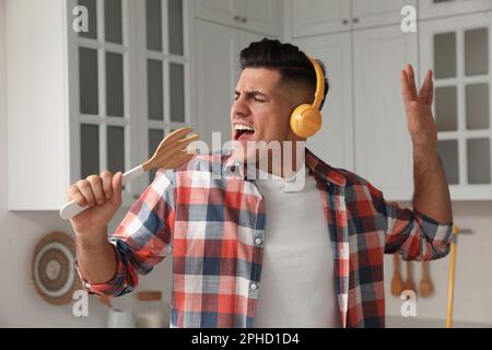 Uomo con cuffie e spatola a forchetta che canta in cucina Foto Stock