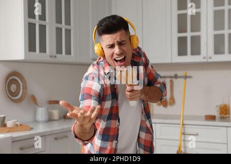 Uomo con cuffie e spatola a forchetta che canta in cucina Foto Stock