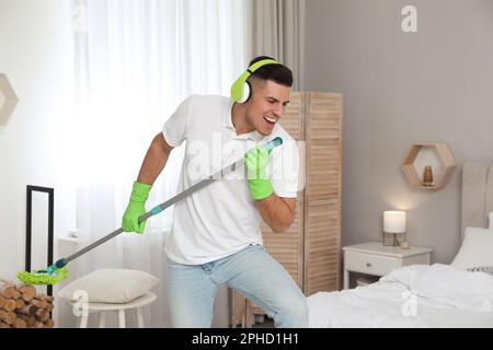 Uomo con il mop che canta mentre pulisce in camera da letto Foto Stock
