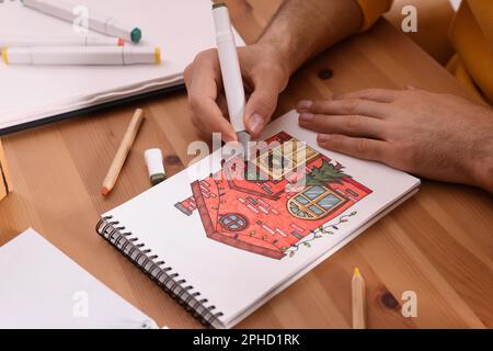 Uomo disegno in un libro di disegno con pennarello a tavola di legno, primo piano Foto Stock