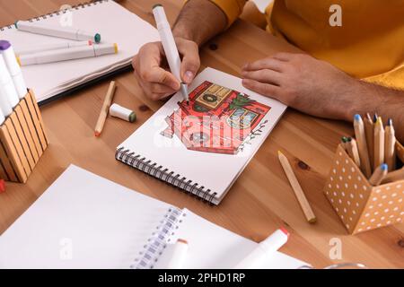 Uomo disegno in un libro di disegno con pennarello a tavola di legno, primo piano Foto Stock