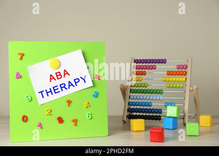 Lavagna magnetica con frase ABA Therapy, numeri colorati e abaco su tavolo di legno bianco Foto Stock