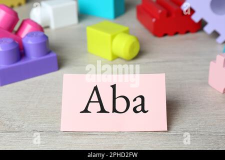 Foglio di carta con abbreviazione ABA (Applied Behavior Analysis) e blocchi di legno colorati su tavola bianca, primo piano Foto Stock