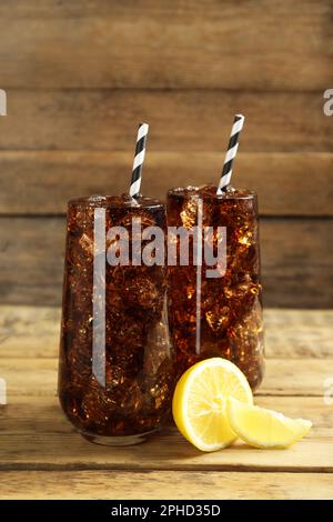 Bicchieri di acqua soda rinfrescante con cubetti di ghiaccio e limone su tavolo di legno Foto Stock
