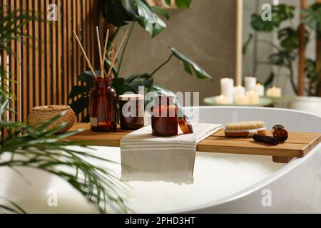 Vassoio da bagno in legno con libro aperto, candela e prodotti per la cura del corpo in vasca interna. Atmosfera rilassante Foto Stock