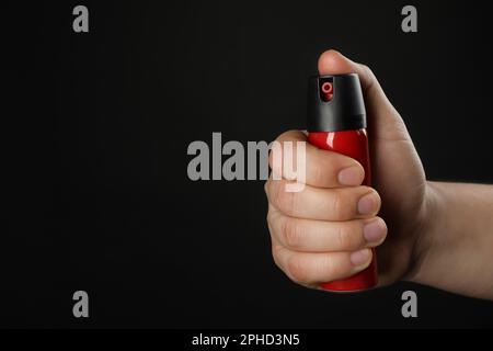 Uomo che tiene pepe spray su sfondo nero, primo piano. Spazio per il testo Foto Stock