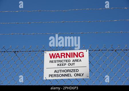 avvertenza aree limitate tenere fuori il personale autorizzato apporre solo un cartello su una recinzione di maglia a catena con sfondo blu Foto Stock