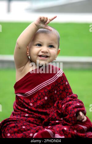 Un simpatico bambino calvo è vestito in avatar Monk, indossando uno scialle di maroon e dando un sorriso carino Foto Stock